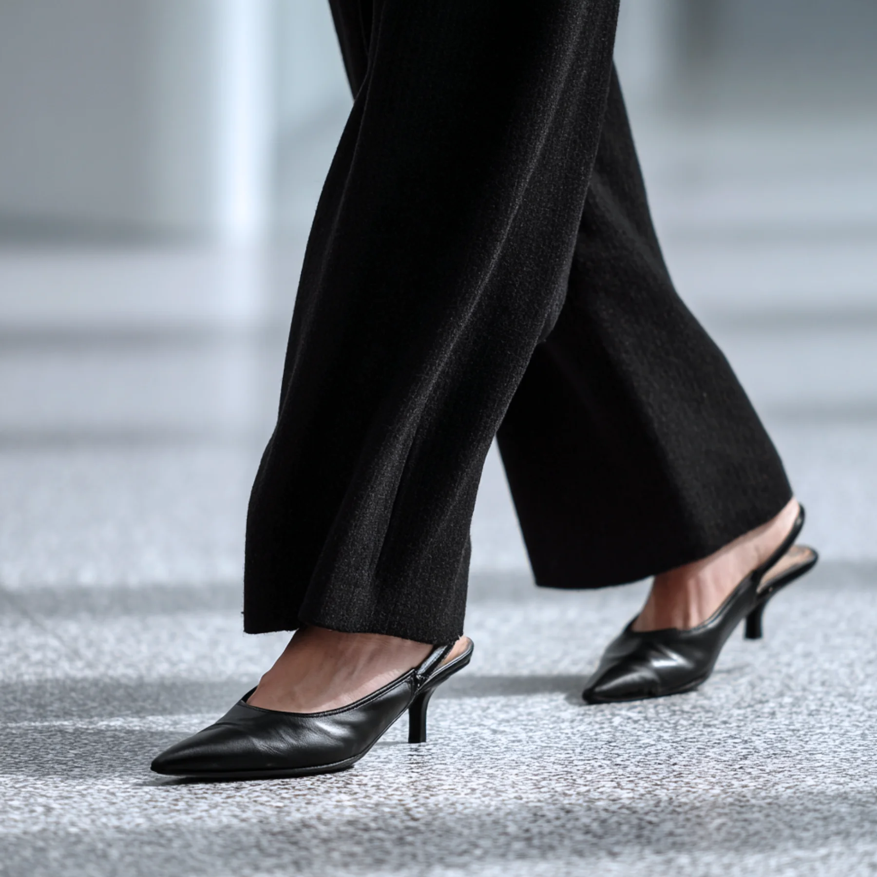 Close-up of a woman mid-stride in black slingback heels and wide-leg trousers — the daily expression of a considered personal style